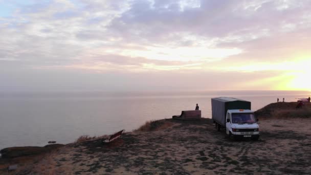 Luftaufnahme eines jungen Mannes, der neben einem Lieferwagen auf einem Hügel steht und bei Sonnenuntergang auf das Meer blickt. Meditation und Reflexion — Stockvideo