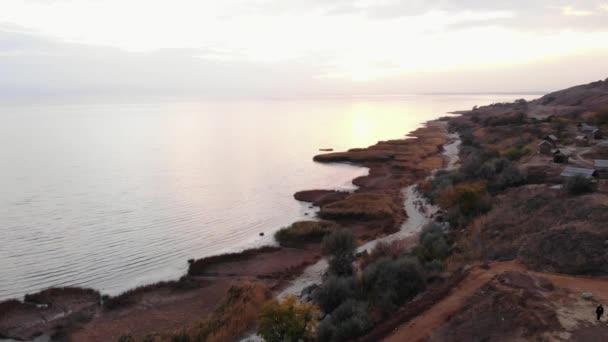 Deniz kıyısının havadan görünüşü ve deniz feneri evlerin ve yolun yanındaki tepede. — Stok video