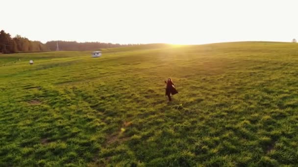 Vista aérea de una joven girando con los brazos extendidos en la puesta del sol en un gran campo verde. Concepto de felicidad — Vídeos de Stock