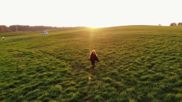 Sparatoria da drone di una giovane ragazza che corre attraverso verdi prati collinari sullo sfondo di un tramonto — Video Stock