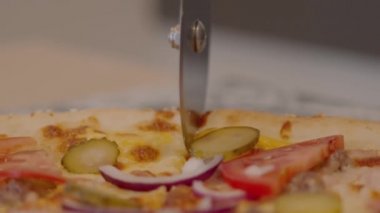 Yuvarlak tekerlekli bıçakla bir kafede çeşitli malzemelerle dilimlenmiş pizzanın yakın çekimi.