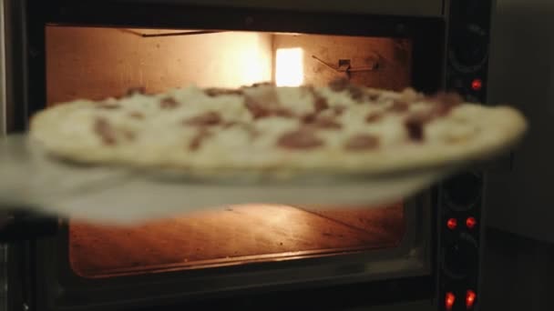 요리사는 빵을 가득 채운 피자를 오븐에 있는 구운 접시 위에 나무로 된 요리용 가문비나무 위에 놓습니다. 클로즈업 — 비디오