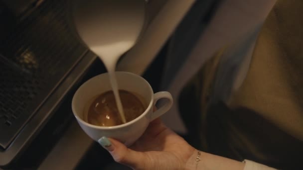 Close-up da mão de uma menina barista que derrama leite batido em uma xícara de café e faz um desenho na superfície — Vídeo de Stock