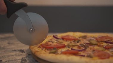 Şef, özel yuvarlak bıçakla bir kafede masasında dolgu olan bir pizzayı dilimliyor. Yakın plan.