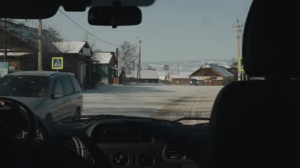 BAIKAL, IRKUTSK REGION, RUSSIA - MARCH 11, 2021: A man drives a car on a winter road past wooden houses against the backdrop of snow-capped mountains. Inside view — Stock Video