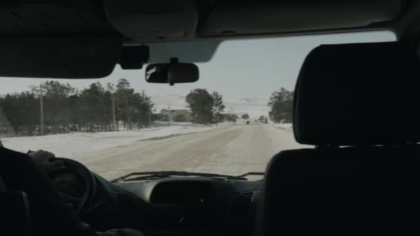 Вид через лобовое стекло автомобиля на зимней дороге среди деревьев на фоне заснеженных гор и неба — стоковое видео