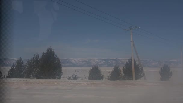Blick aus dem Autofenster auf die schneebedeckten Berge und ein Feld mit Bäumen an einem bewölkten Wintertag — Stockvideo