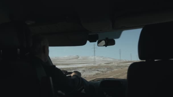 Bir kış günü, geniş bir yolda araba süren bir adam karlı dağların arka planına çarpıyor. Ön camdan bak. — Stok video