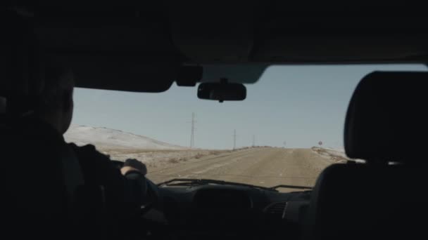 Un hombre que conduce un coche conduce a lo largo de una carretera ancha en un día de invierno contra el telón de fondo de las montañas nevadas. Vista a través del parabrisas — Vídeos de Stock