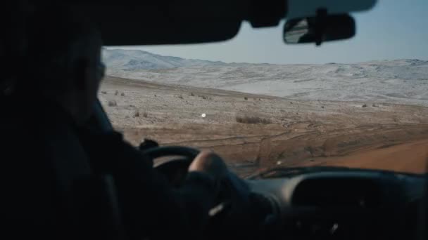 Un hombre conduce un coche contra el telón de fondo de montañas nevadas en el camino al lago Baikal como parte de un viaje de invierno. Vista interior — Vídeos de Stock