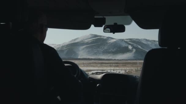 Arabanın ön camından gökyüzünün arka planındaki karla kaplı geniş sıradağlara bakın. Kış yolculuğu konsepti — Stok video