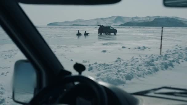 Una vista a través del parabrisas de un coche a la gente que monta tubería atada a un automóvil en el hielo congelado del lago Baikal — Vídeos de Stock