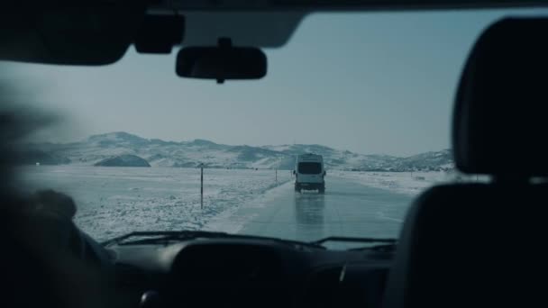 Minibussen rijden langs de ijzige weg van bevroren Baikalmeer tegen de achtergrond van de capes van Olkhon Island — Stockvideo