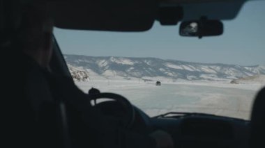 Karla kaplı dağ sıralarıyla çevrili donmuş Baykal Gölü 'nün buzuna giden yolun ön camından bakın. Kış yolculuğu