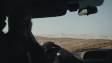 Yoldaki bir arabanın ön camından karla kaplı dağların güzel manzarası. Kış yolculuğu konsepti
