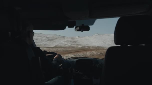 BAIKAL, IRKUTSK REGION, RUSSIA - 11 Mart 2021: Toprak bir yolda bir arabanın ön camından bakın ve kış dağlarının arka planından geçen bir araba — Stok video