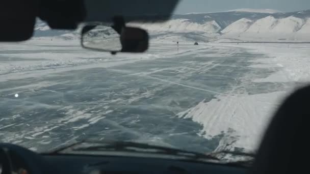 Blick durch die Windschutzscheibe eines Autos auf Menschen und andere Autos auf dem gefrorenen Eis des von Bergen umgebenen Baikalsees — Stockvideo