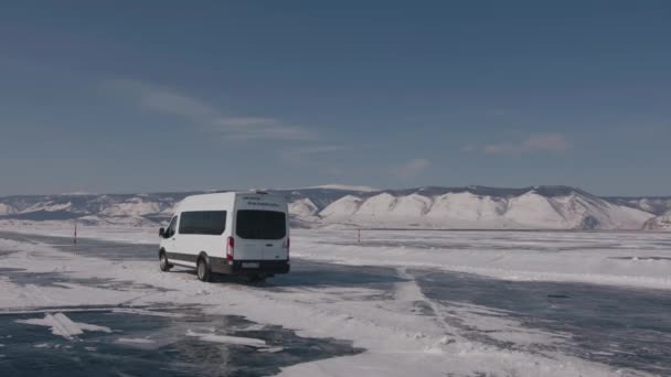 BAIKAL, IRKUTSK REGION, RUSSIA - 18 marca 2021: Widok minibusów przejeżdżających na lodzie jeziora Bajkał otoczony śnieżnymi pasmami górskimi podczas zimowych wycieczek — Wideo stockowe