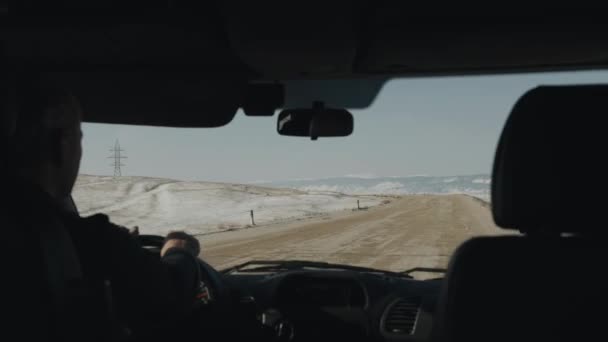 Un hombre conduce un coche a lo largo de una amplia carretera en las estribaciones del lago Baikal en un día nublado de invierno. Vista a través del parabrisas — Vídeos de Stock