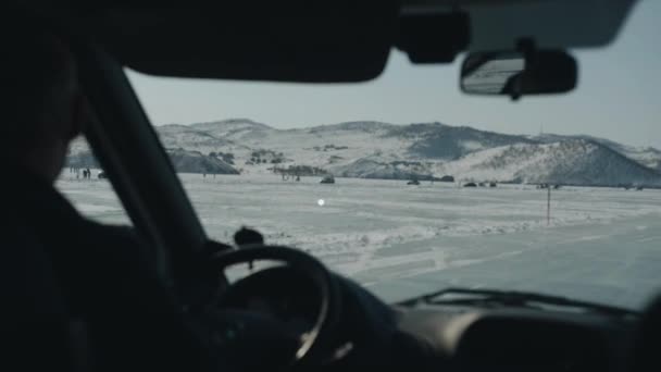 Groups of people and cars on the frozen ice of Lake Baikal against the backdrop of snow-capped mountains during a winter trip — Stock Video