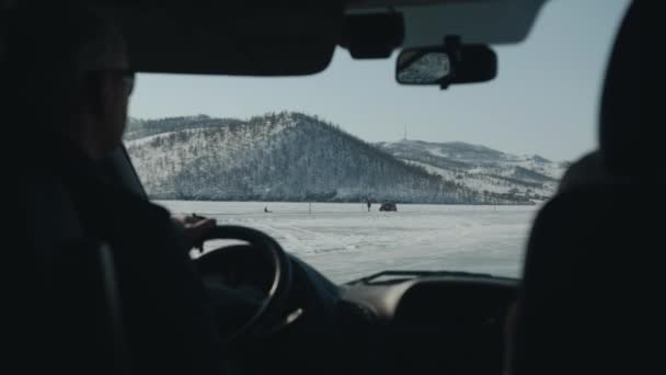 Utsikt genom vindrutan på en bil på den frusna sjön Baikal mot bakgrund av bergskläderna på Olkhon Island — Stockvideo