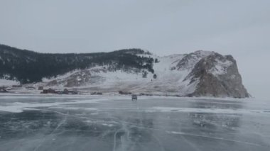Baykal Gölü 'nün donmuş buzu üzerinde dağların eteklerindeki bir yerleşim yerine giden bir UAZ minibüsünün görüntüsü.