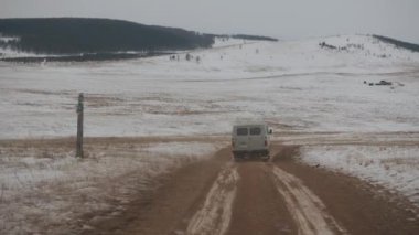 UAZ minibüsü Baykal Gölü eteklerindeki toprak bir yoldan karla kaplı bir köye gidiyor.