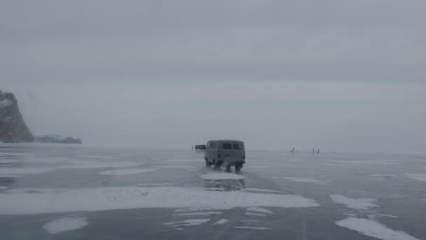 A UAZ minibus carries tourists across the frozen ice of Lake Baikal past mountains and groups of people and cars — Stock Video