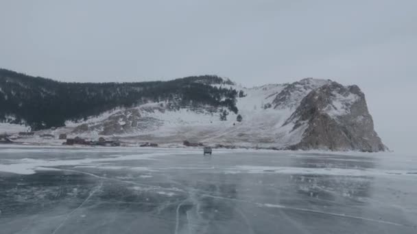 Baykal Gölü 'nün donmuş buzu üzerinde dağların eteklerindeki bir yerleşim yerine giden bir UAZ minibüsünün görüntüsü. — Stok video