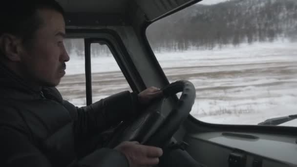 바이칼, 이르쿠츠크 지역, 2021 년 3 월 18 일: 비야트 운전자가 바이칼호에 있는 UAZ 미니버스 운전대 뒤에서 관광객을 태우고 바이칼호를 배경으로 이동하다 — 비디오