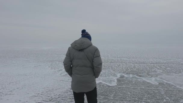 Baikal, Región de Irkutsk, Rusia - 18 de marzo de 2021: Un hombre se para en la cima de una montaña y mira el lago cubierto de hielo Baikal. El concepto de libertad en uno con uno mismo — Vídeo de stock