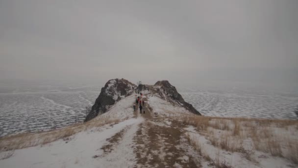 Un grupo de turistas camina a lo largo del camino hacia el cabo con una vista impresionante de la extensión del lago congelado Baikal — Vídeo de stock