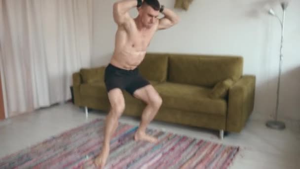 Young muscular man in black shorts plays sports at home and does exercises on the mat during coronavirus quarantine — Stock Video