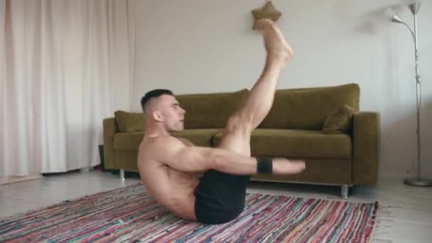 Hombre joven guapo entrenando en su habitación y haciendo ejercicio abdominal mientras está acostado en la alfombra. Deporte en cuarentena — Vídeo de stock