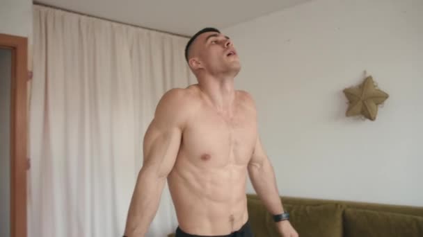 トレーニングの前に裸の胴を持つ筋肉の若い男が伸び、彼の部屋でスクワットやスイング足を行います — ストック動画