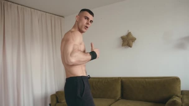 Hombre joven musculoso guapo haciendo ejercicio en casa y haciendo ejercicios abdominales en la estera mostrando el pulgar hacia arriba — Vídeo de stock