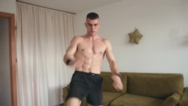 Hombre joven musculoso guapo entrenando en casa en cuarentena durante la pandemia del coronavirus. Concepto de vida saludable — Vídeo de stock