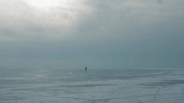 两个人骑在白加尔湖结冰的冰上，冰上布满了裂缝和雪。积极的假日和冬季旅行概念 — 图库视频影像