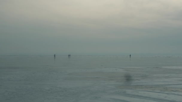 Skupina lidí chodí a bruslí na zamrzlém a zasněženém povrchu jezera Bajkal za oblačného zimního dne — Stock video