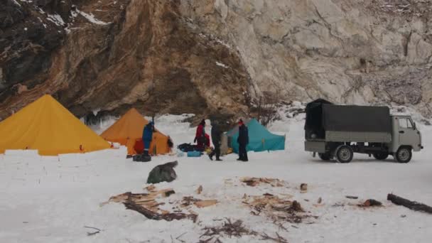 Baikal, Región de Irkutsk, Rusia - 18 de marzo de 2021: Un grupo de personas coloca las cosas en una furgoneta UAZ en un campamento de campaña en el hielo congelado del lago baikal al pie de la montaña — Vídeo de stock