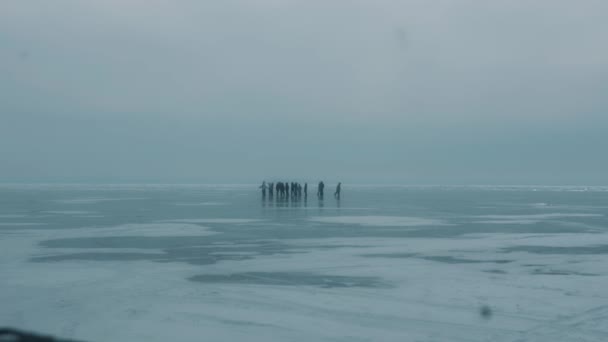 Skupina lidí na průhledném ledě zamrzlého jezera bajkalské procházky a bruslí v zamračený den — Stock video