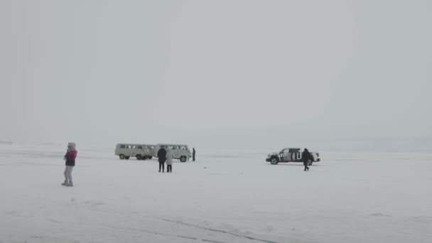Baikal, regio Irkoetsk, Rusland - 18 maart 2021: Minibussen UAZ en een pick-up truck staan op het ijs van het Baikalmeer en een groep mensen die over het bevroren oppervlak lopen — Stockvideo