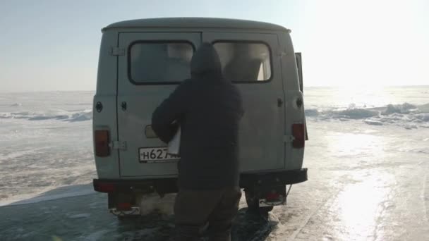 Baikal, Region Irkutsk, Russland - 18. März 2021: Ein Mann öffnet die Hintertür eines UAZ-Kleinbusses und legt während einer Fahrt auf dem zugefrorenen Baikalsee Dinge dort ab. — Stockvideo