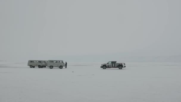 Minibuses UAZ y una camioneta en el hielo del lago Baikal y un grupo de personas caminando sobre la superficie congelada — Vídeo de stock