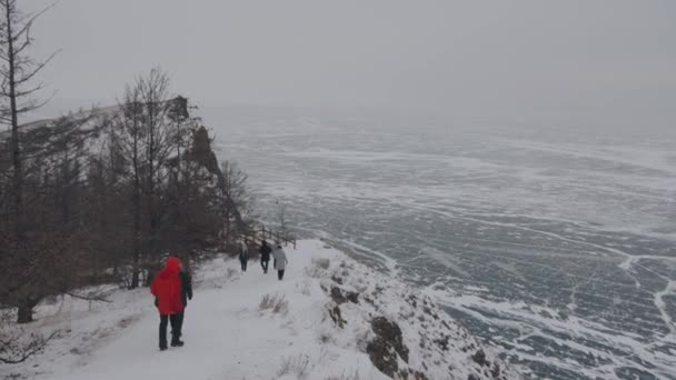 En grupp människor stiger ner från berget längs en snötäckt stig till den istäckta sjön Baikal — Stockvideo