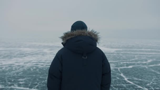 Um homem está no topo de uma montanha e olha para o lago congelado Baikal. Sensação de liberdade e poder ilimitado. Visão traseira — Vídeo de Stock