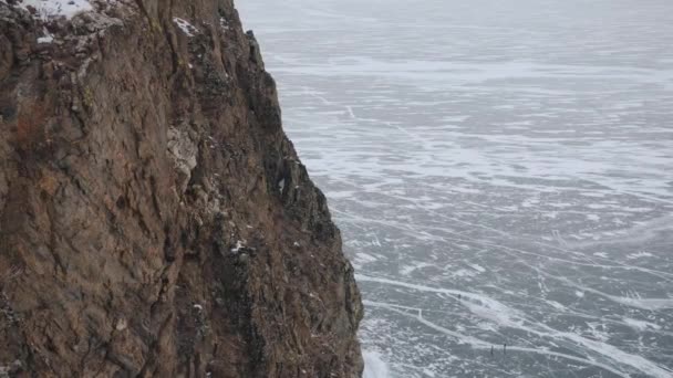 Vista das montanhas costeiras para o gelo rachado do Lago Baikal e as pessoas no sopé do penhasco — Vídeo de Stock