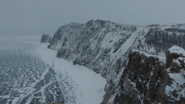 Een prachtig uitzicht op de bergen begroeid met bos aan de oever van het bevroren Baikalmeer op een besneeuwde winterdag — Stockvideo