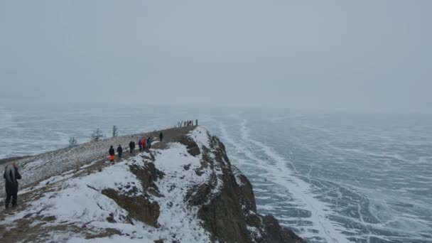 Eine Touristengruppe wandert zum Rand einer Klippe am Ufer und einem mit Eis bedeckten Blick auf den Baikalsee — Stockvideo