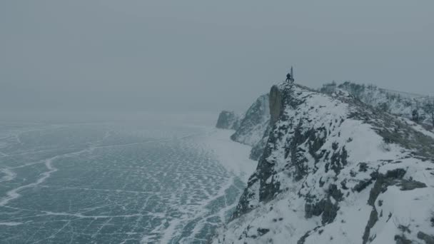 Dos hombres se paran en lo alto de un acantilado en la costa del congelado lago Baikal y disfrutan de la sensación de libertad y el poder de la naturaleza — Vídeo de stock